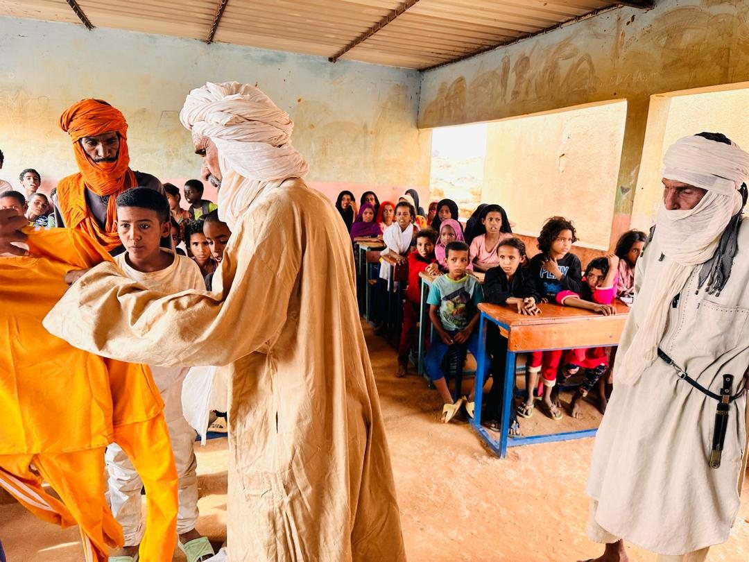 A pupil tries on his new outfit, watched by his classmates and the elders.
