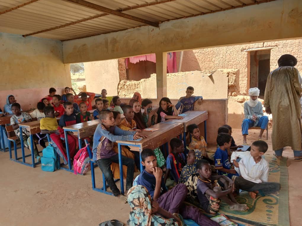 With not enough benches for everyone, some pupils follow the lesson sitting on mats.